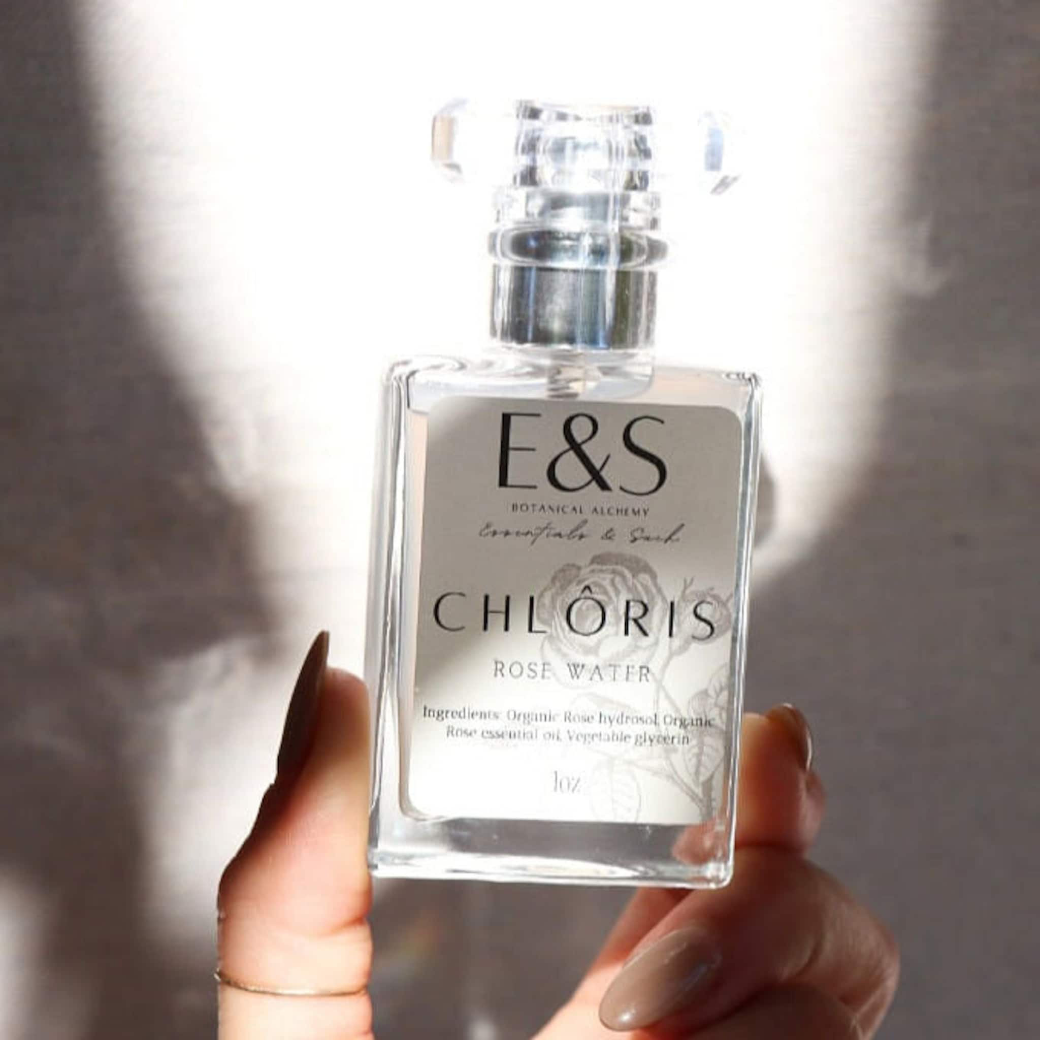 Rose water bottle with clear glass, silver cap, and E&S label held by hand