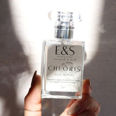 Rose water bottle with clear glass, silver cap, and E&S label held by hand
