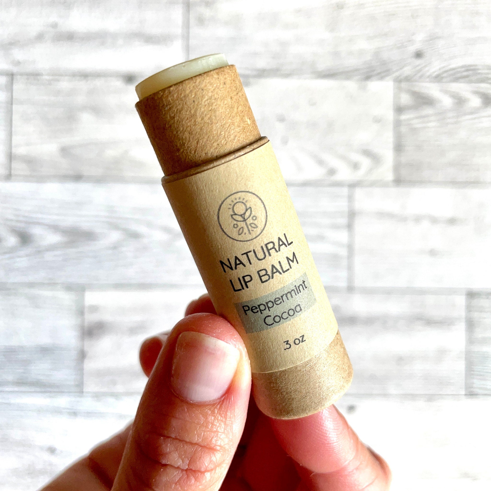 Lip balm tube in tan cardboard with green and white text, held in hand