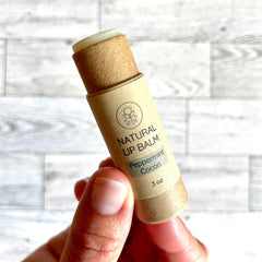 Lip balm tube in tan cardboard with green and white text, held in hand