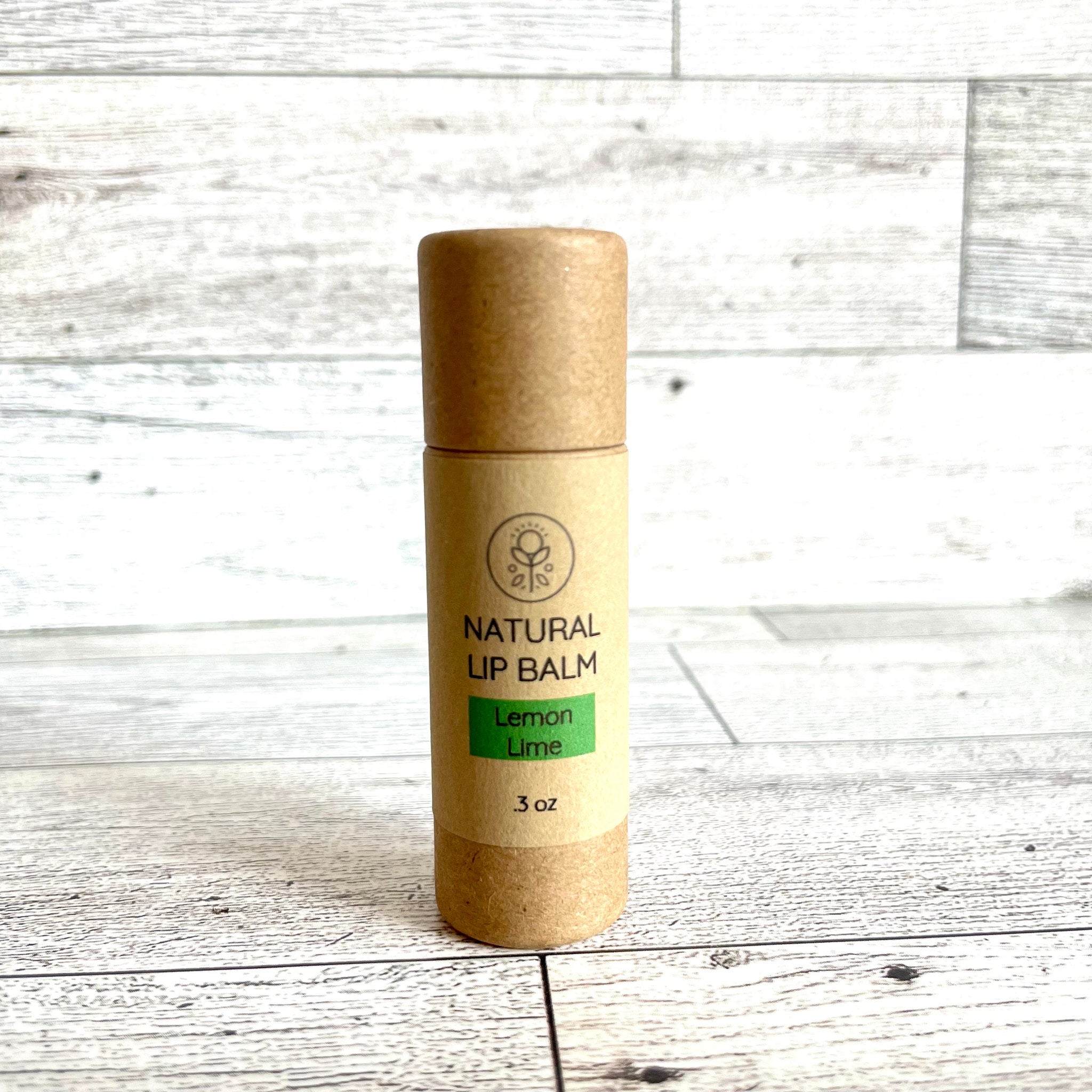 Lip balm tube, brown cardboard, green label, "Natural Lip Balm" text visible