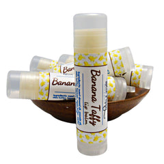 Lip balm tubes with banana pattern, white and yellow, in a wooden bowl, Blue Poppy brand visible