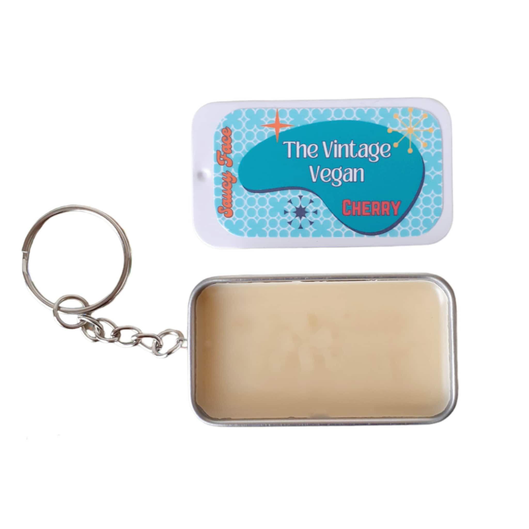 Lip balm tin with white, blue, and silver details, with "Saucy Face" and "The Vintage Vegan" text