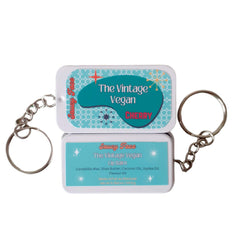 Lip balm tin with teal and white pattern, "Saucy Face" branding, and keychain ring attached