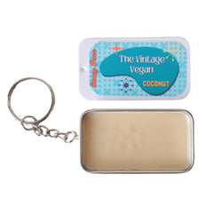 Keychain with Saucy Face branding, metal ring, light brown balm in a metal tin, and blue and white label.