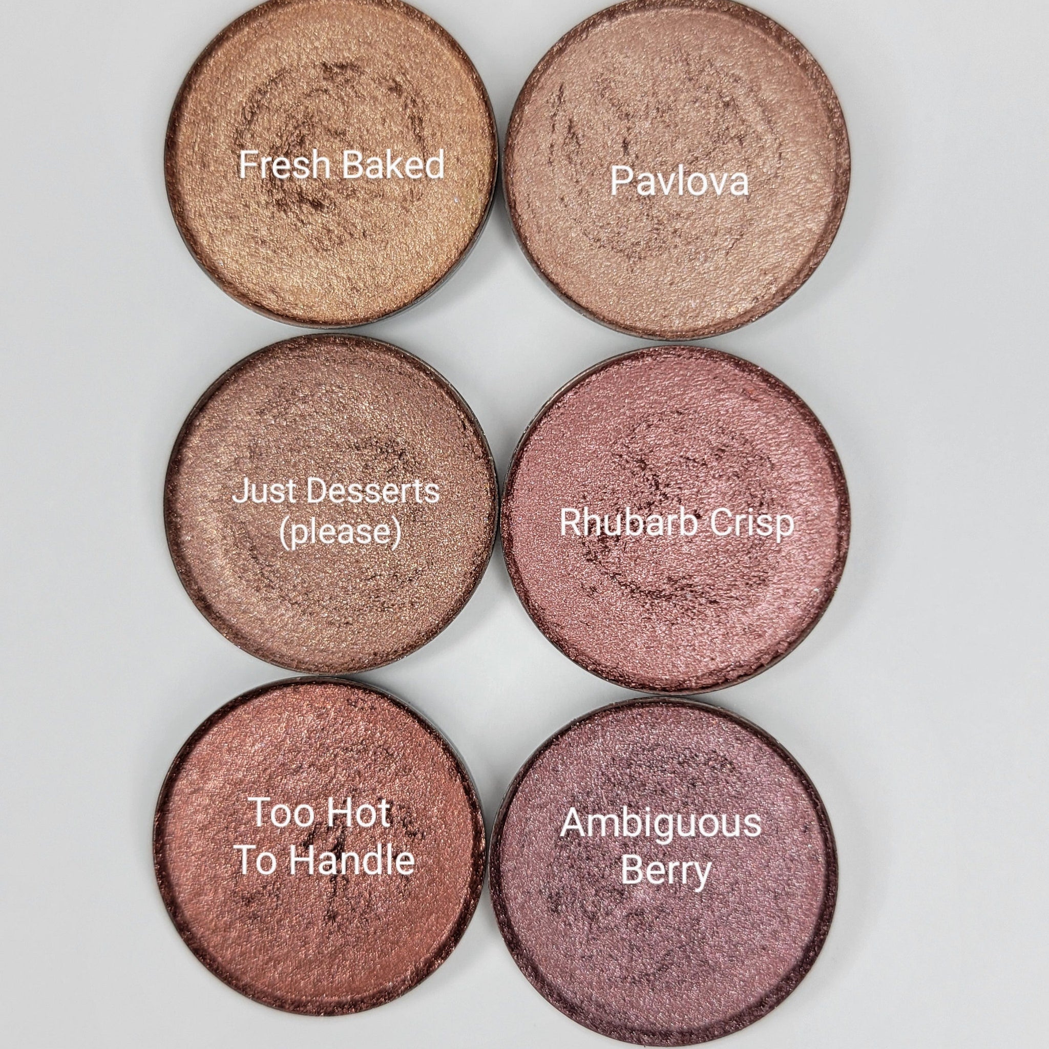 Six shimmer eyeshadow pans in pink, brown, and red hues arranged in a sleek black palette