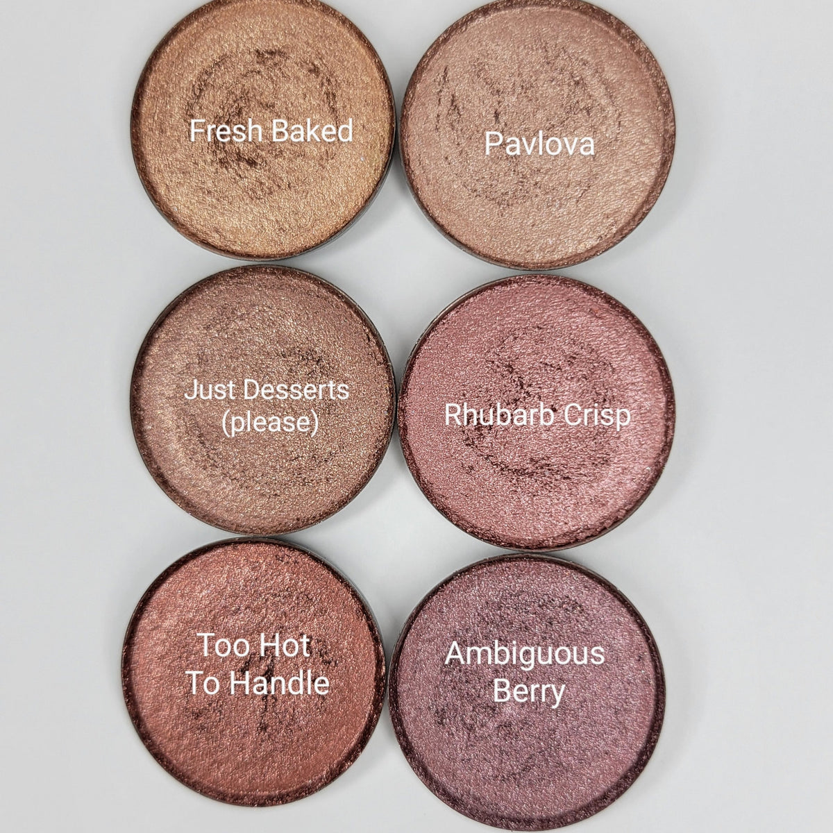 Six shimmer eyeshadow pans in pink, brown, and red hues arranged in a sleek black palette