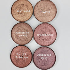 Six shimmer eyeshadow pans in pink, brown, and red hues arranged in a sleek black palette