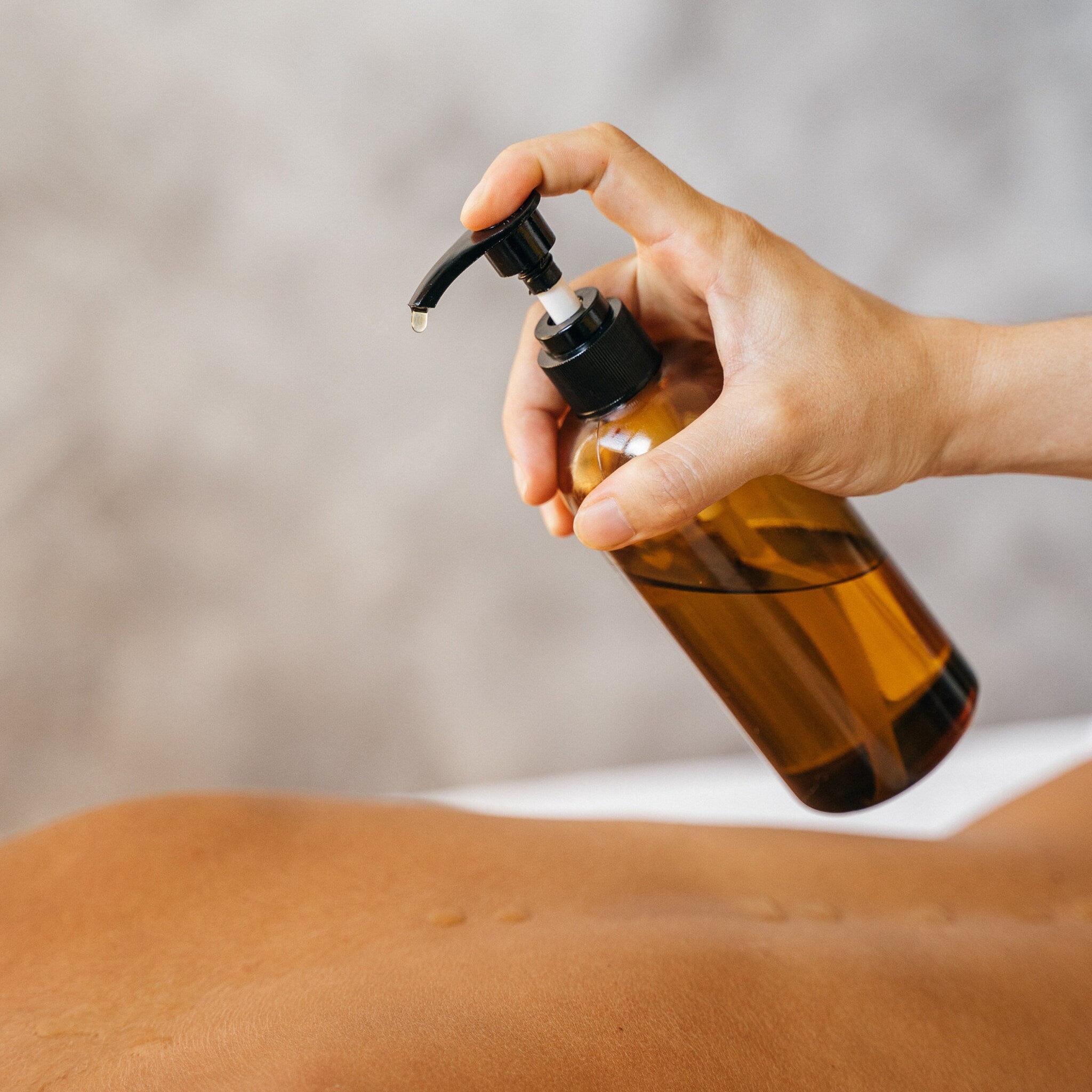 Massage oil bottle dispensing amber glass oil onto skin