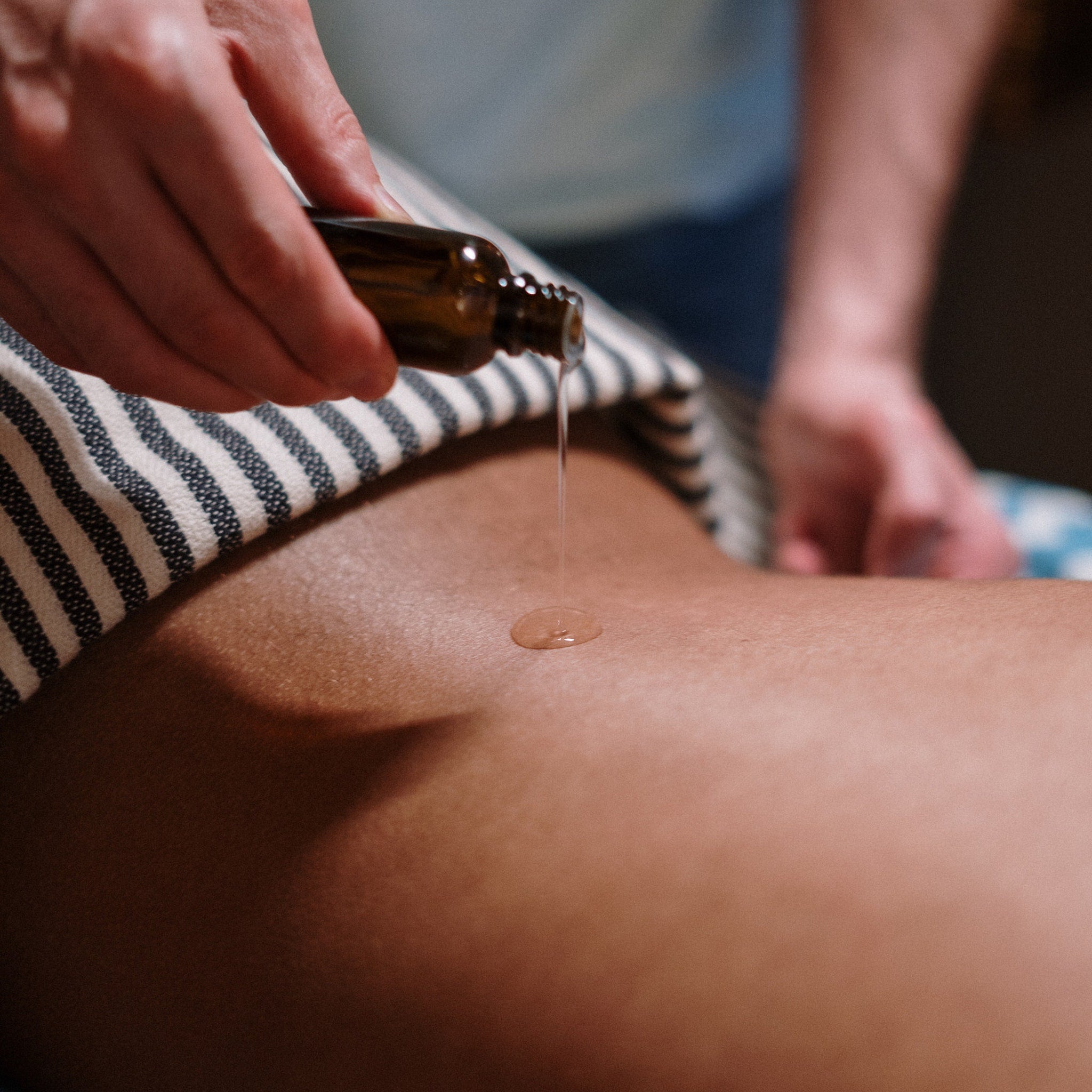 Massage oil being poured, brown bottle, clear liquid, striped towel visible