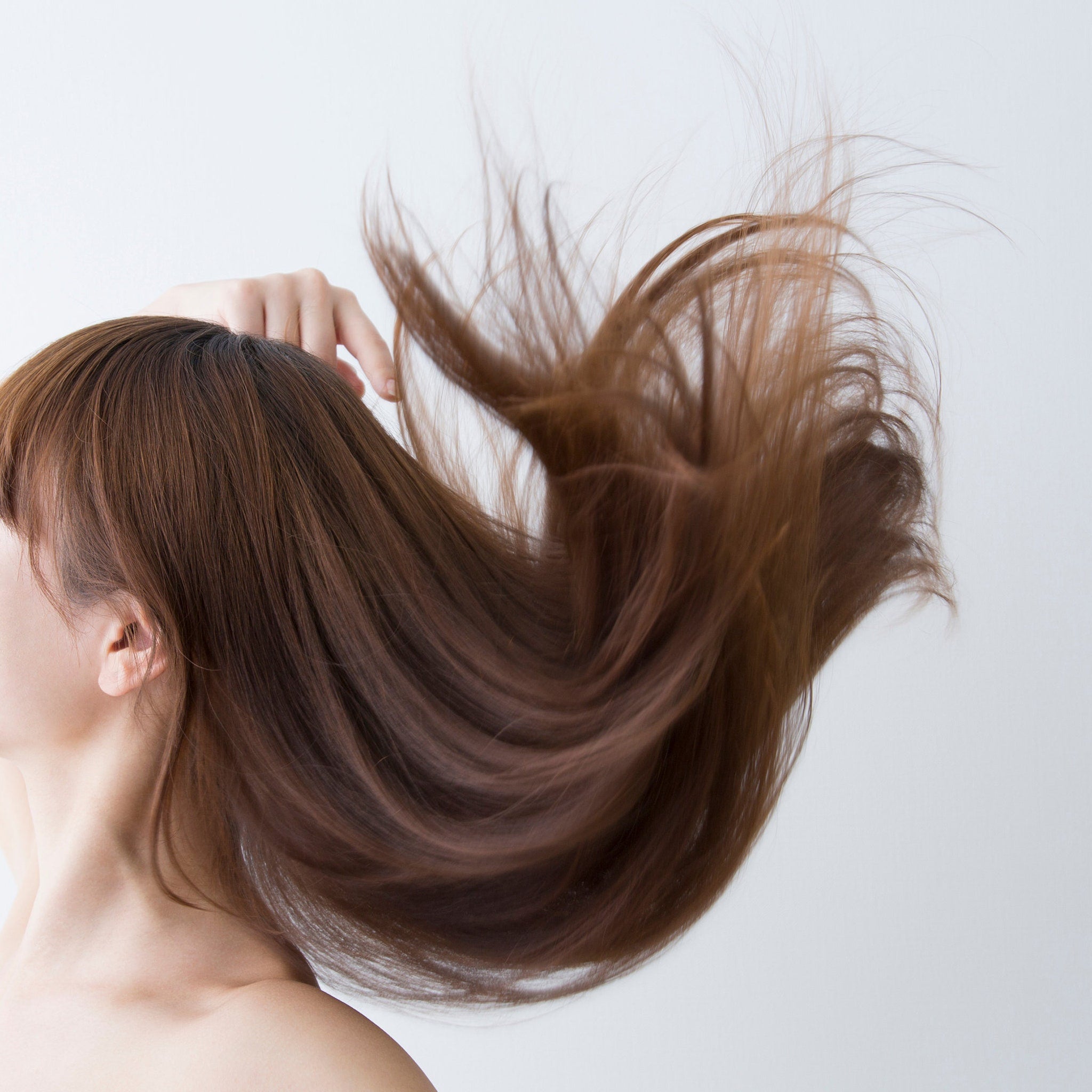 Brown hair flowing in the wind, with a hand touching the hair, showing the side profile of a person