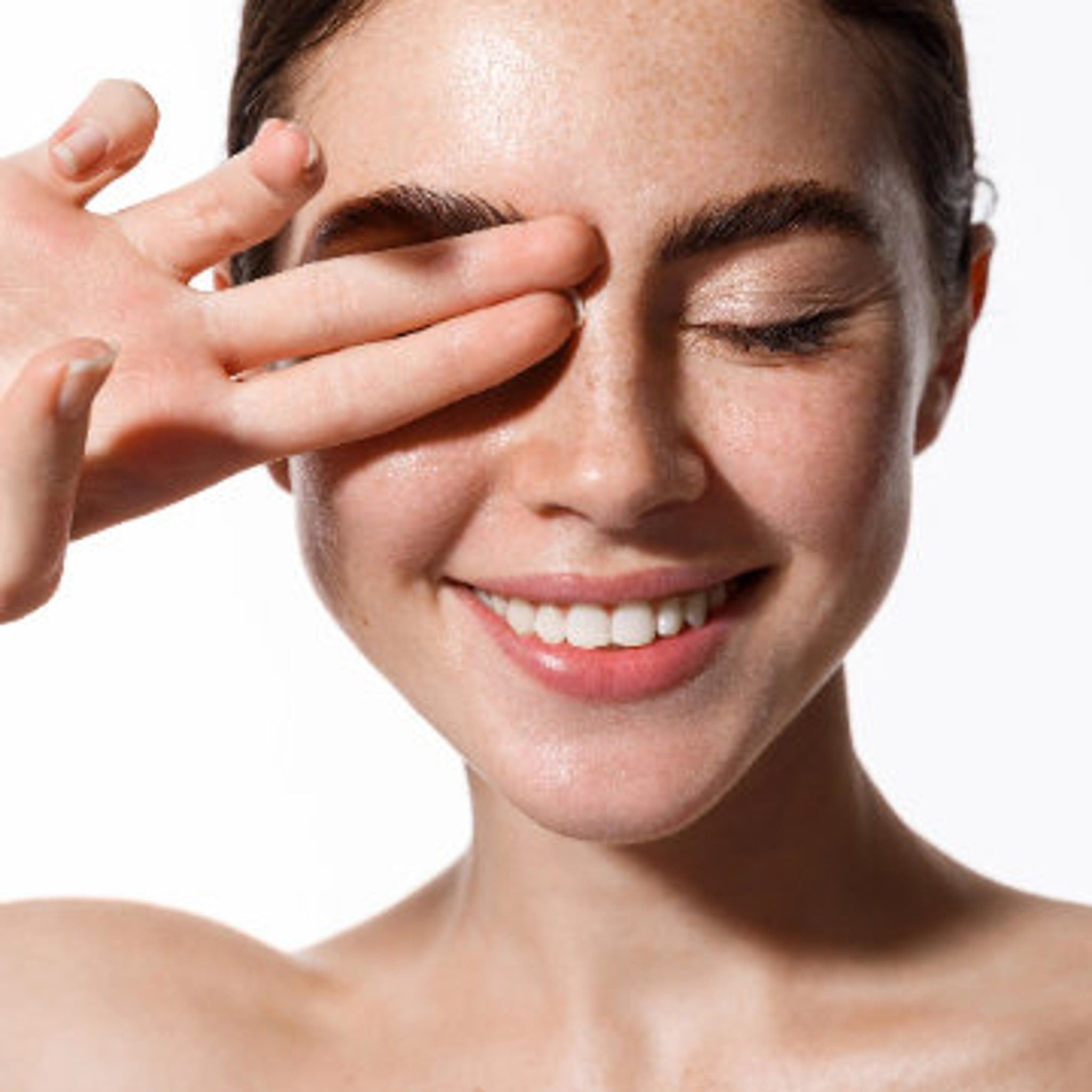 Woman's face with closed eyes, fair skin, and hand covering eye in a smiling pose