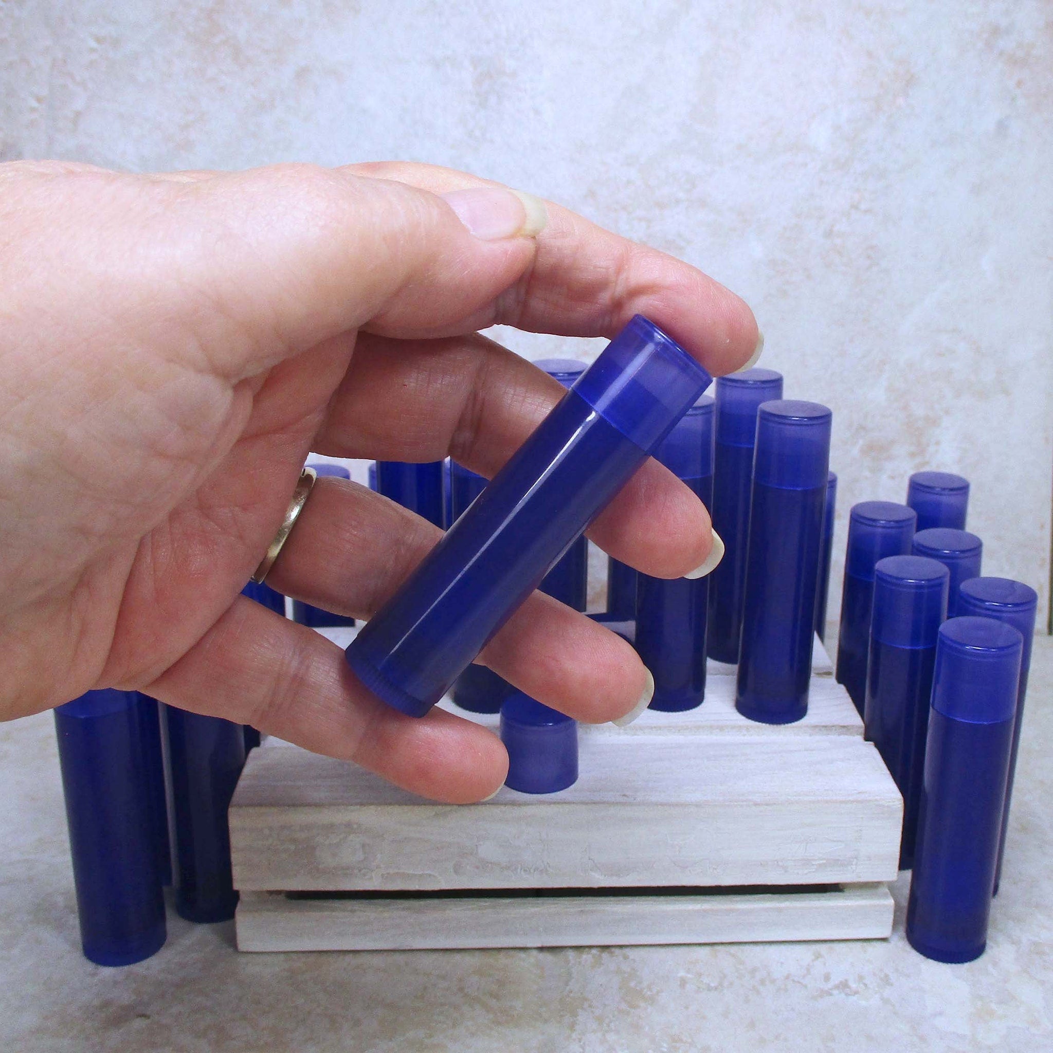 Lip balm tubes, translucent blue plastic, held in hand, with others in background