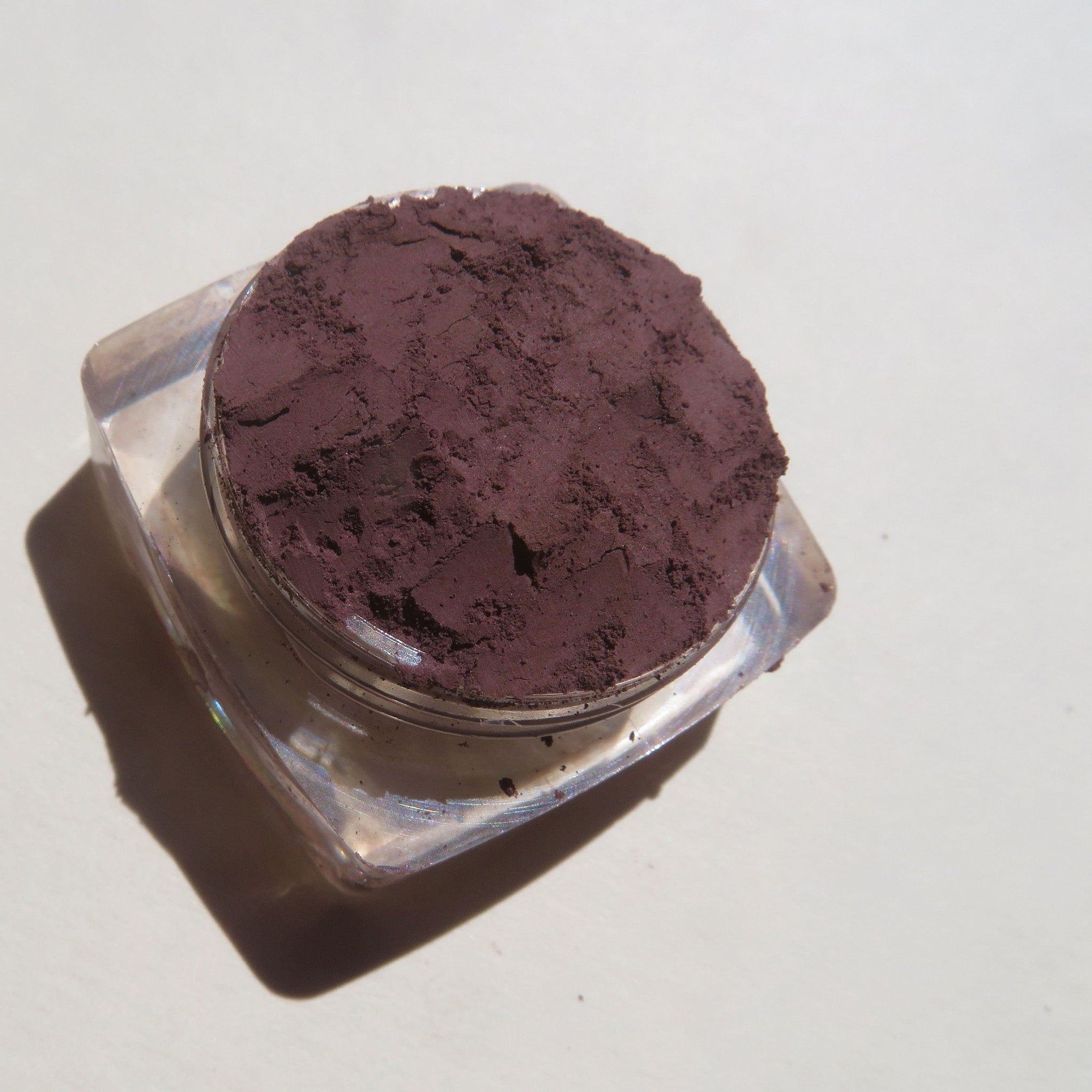 Side view of loose dark purple mineral eyeshadow powder in open jar with matte finish