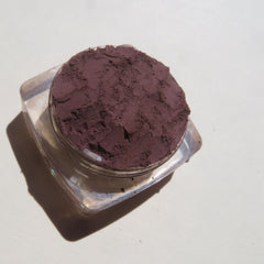 Side view of loose dark purple mineral eyeshadow powder in open jar with matte finish