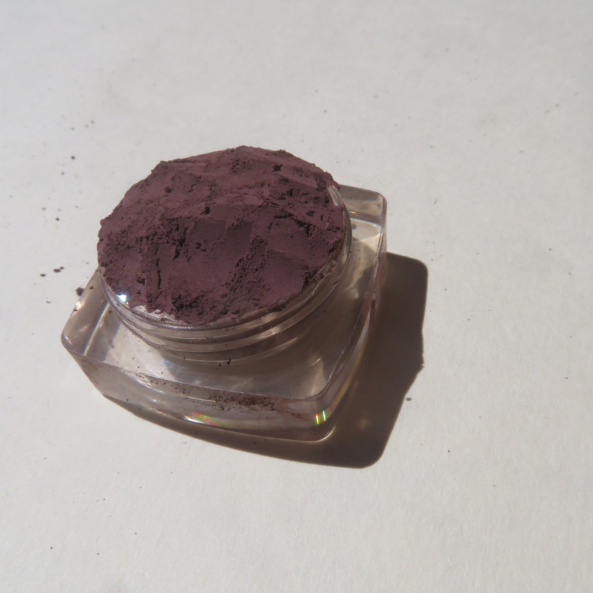 Hand applying dark muted purple loose pigment eyeshadow with a fluffy brush for a soft matte finish
