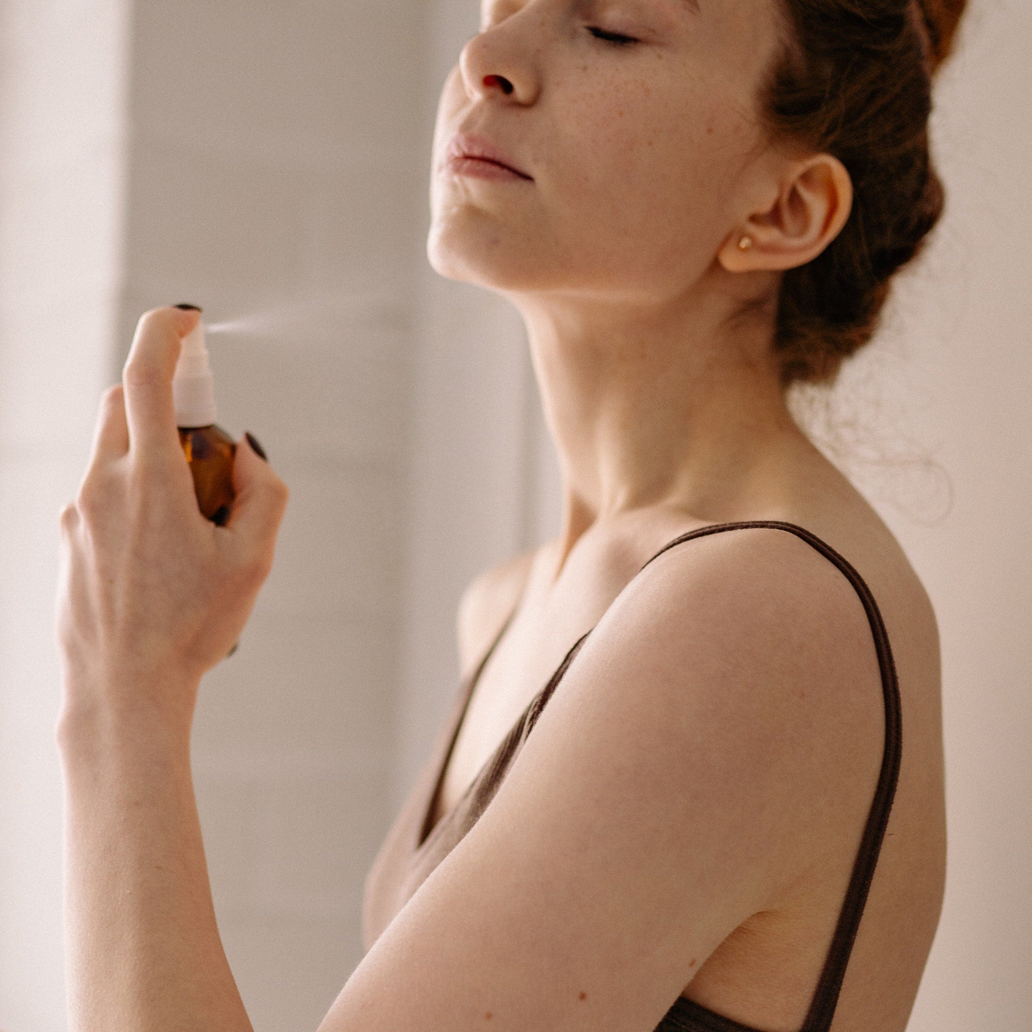 Spray bottle with brown glass, white spray, and woman spraying face