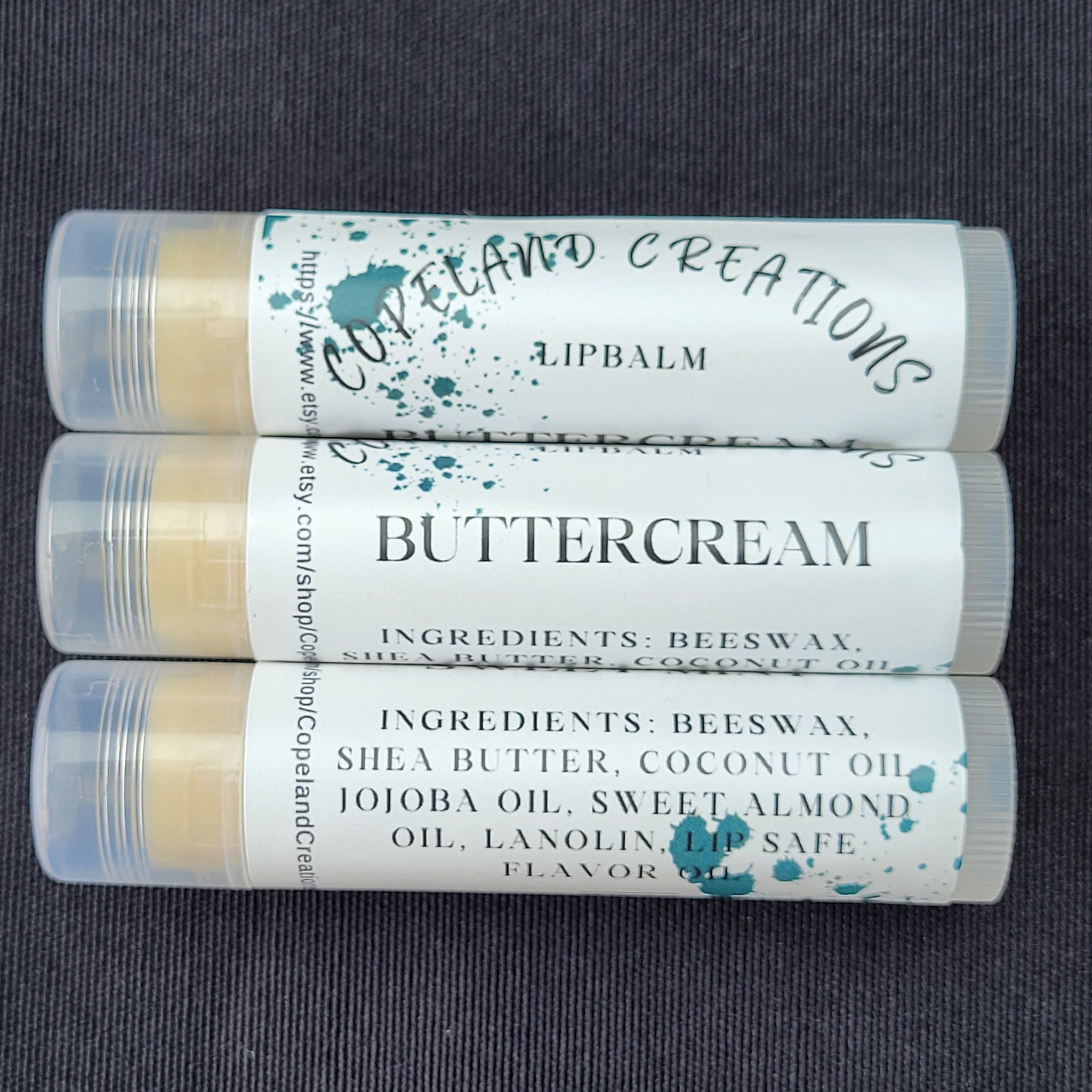 Lip balm tubes with white labels, teal splatter design, and Copeland Creations text visible on a dark surface.