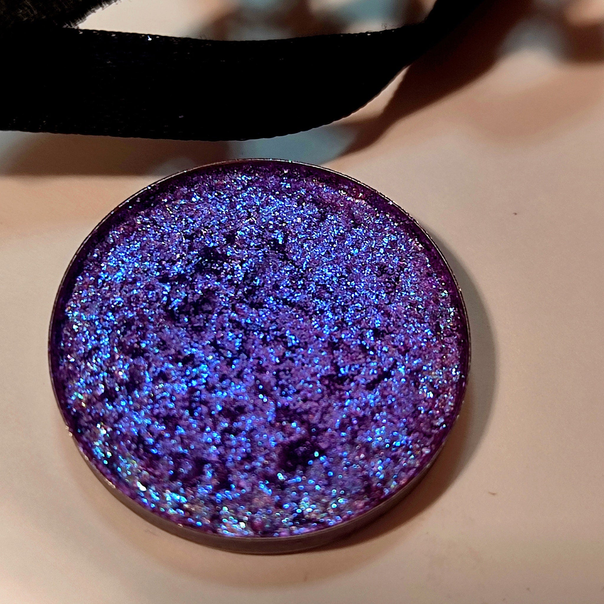 Side view of Uva Eye Shadow compact showcasing its sleek black case and shimmering purple powder texture