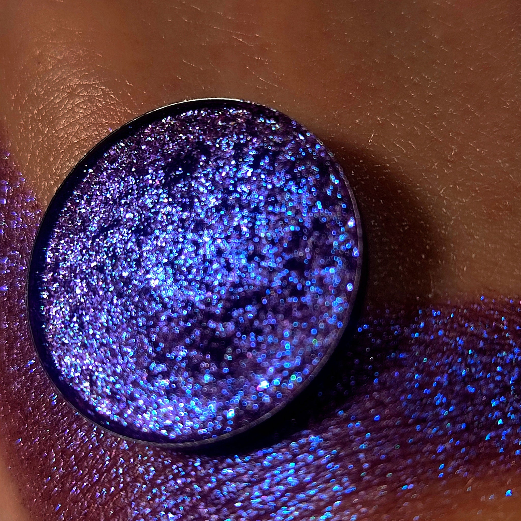 Eyeshadow, round compact with purple glitter, applied on skin, close-up shot