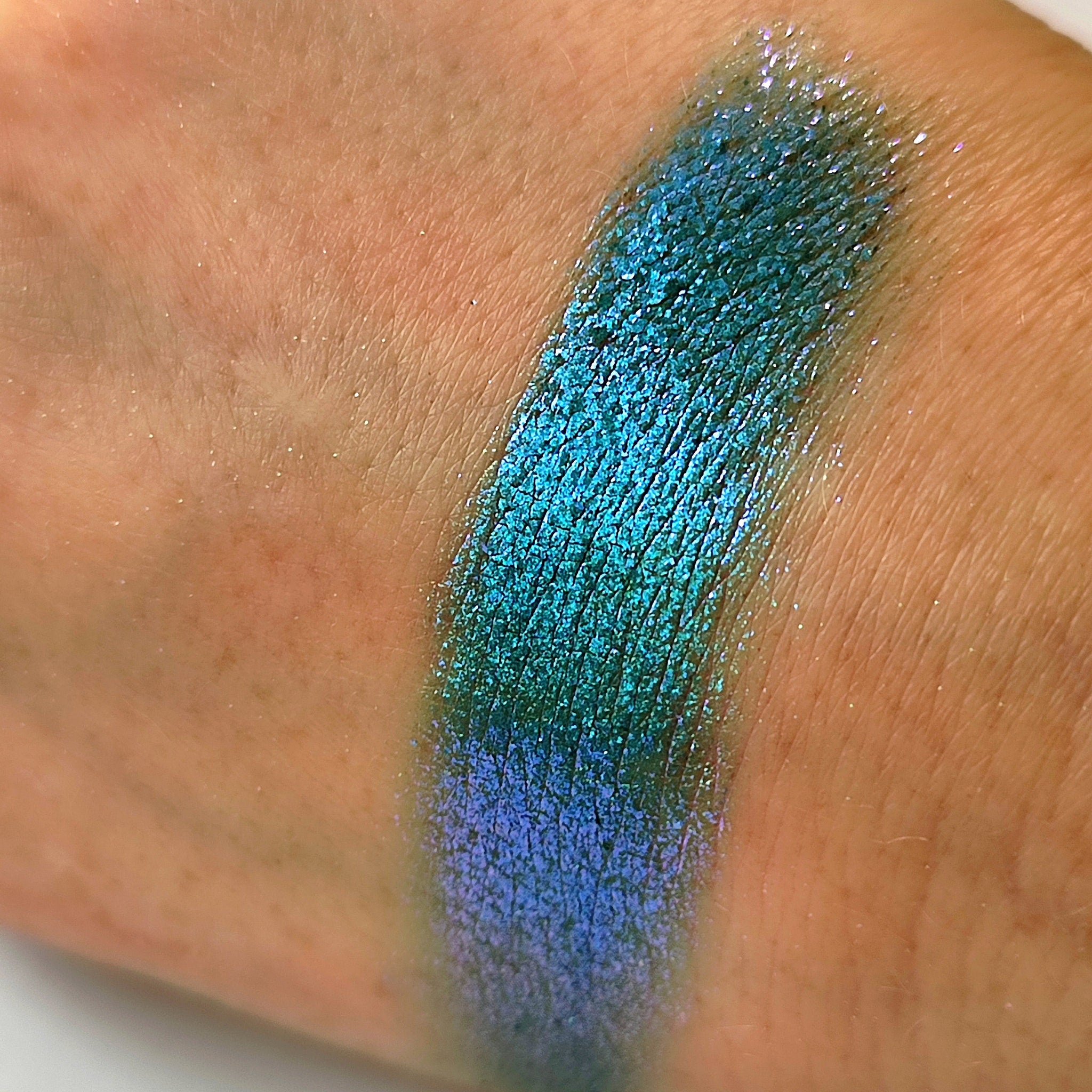 Eyeshadow swatch with teal and blue shimmer on skin, showing color and texture