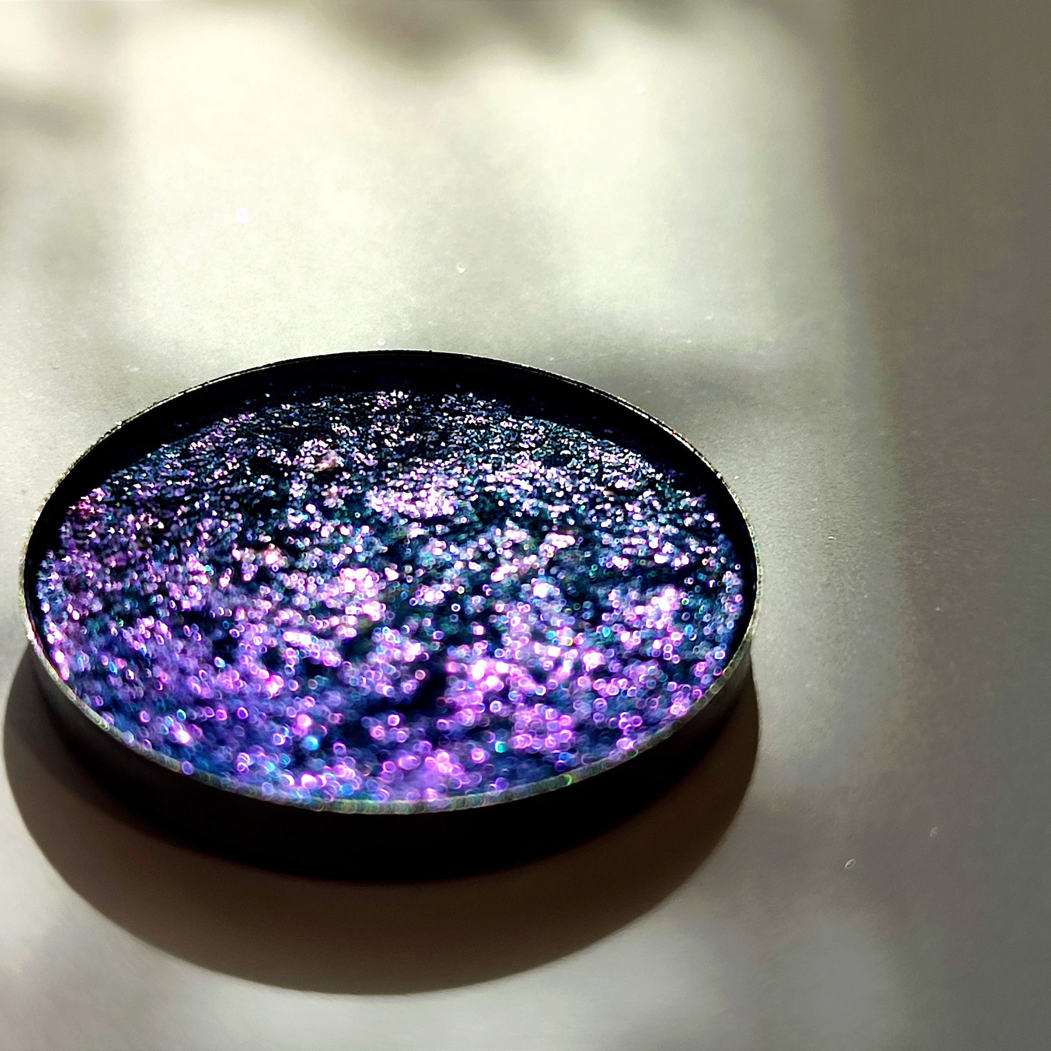 Glitter eyeshadow palette with purple, blue, and silver shimmer in a round metal compact