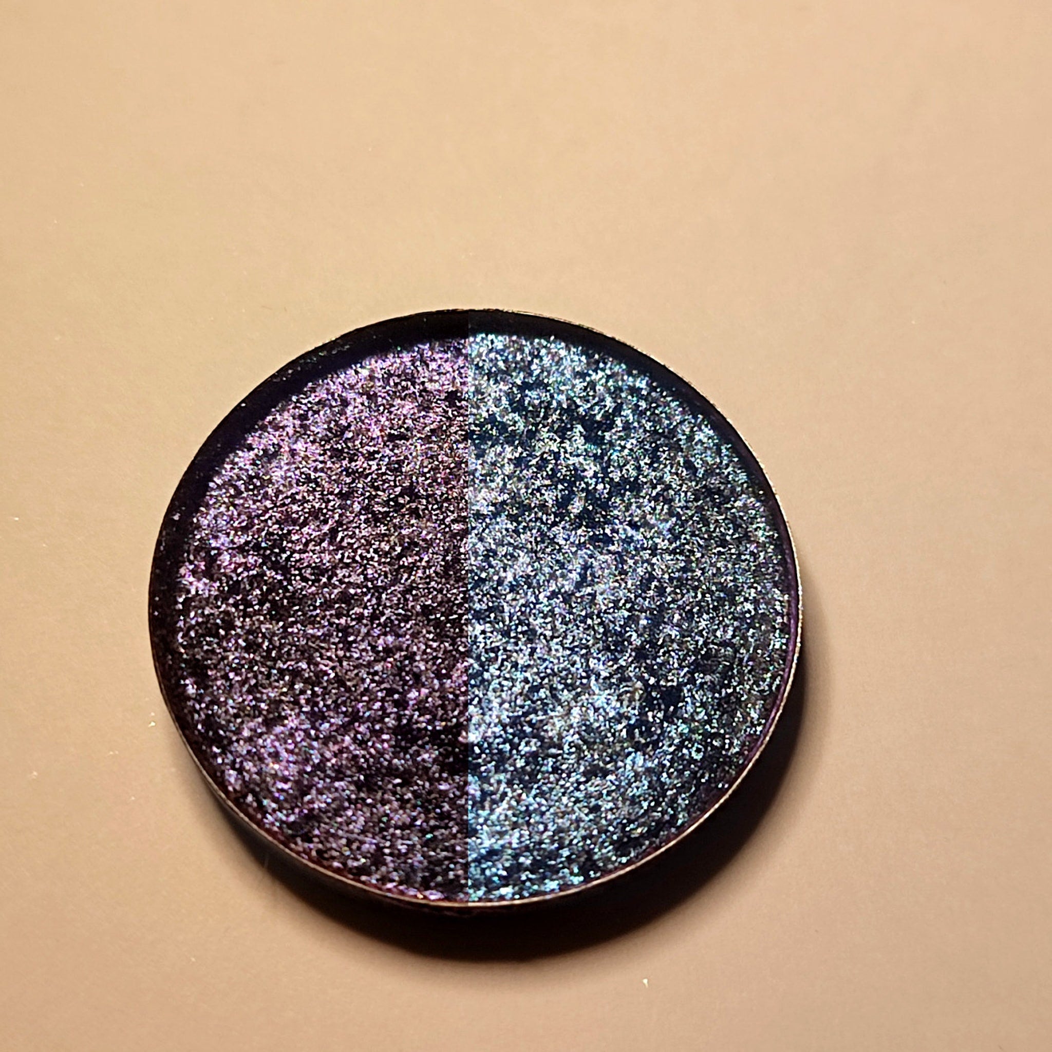 Eyeshadow compact with two-tone iridescent shimmer, dark rim, and round shape