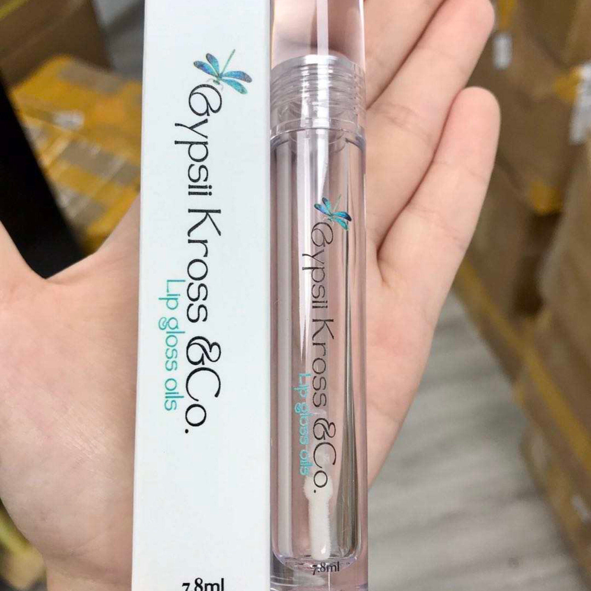 Lip gloss oil, clear tube, white label, Gypsii Kross & Co. branding, held in hand