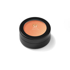 Close-up of fingers applying shimmery bronze eye shadow to eyelid with soft blending brush