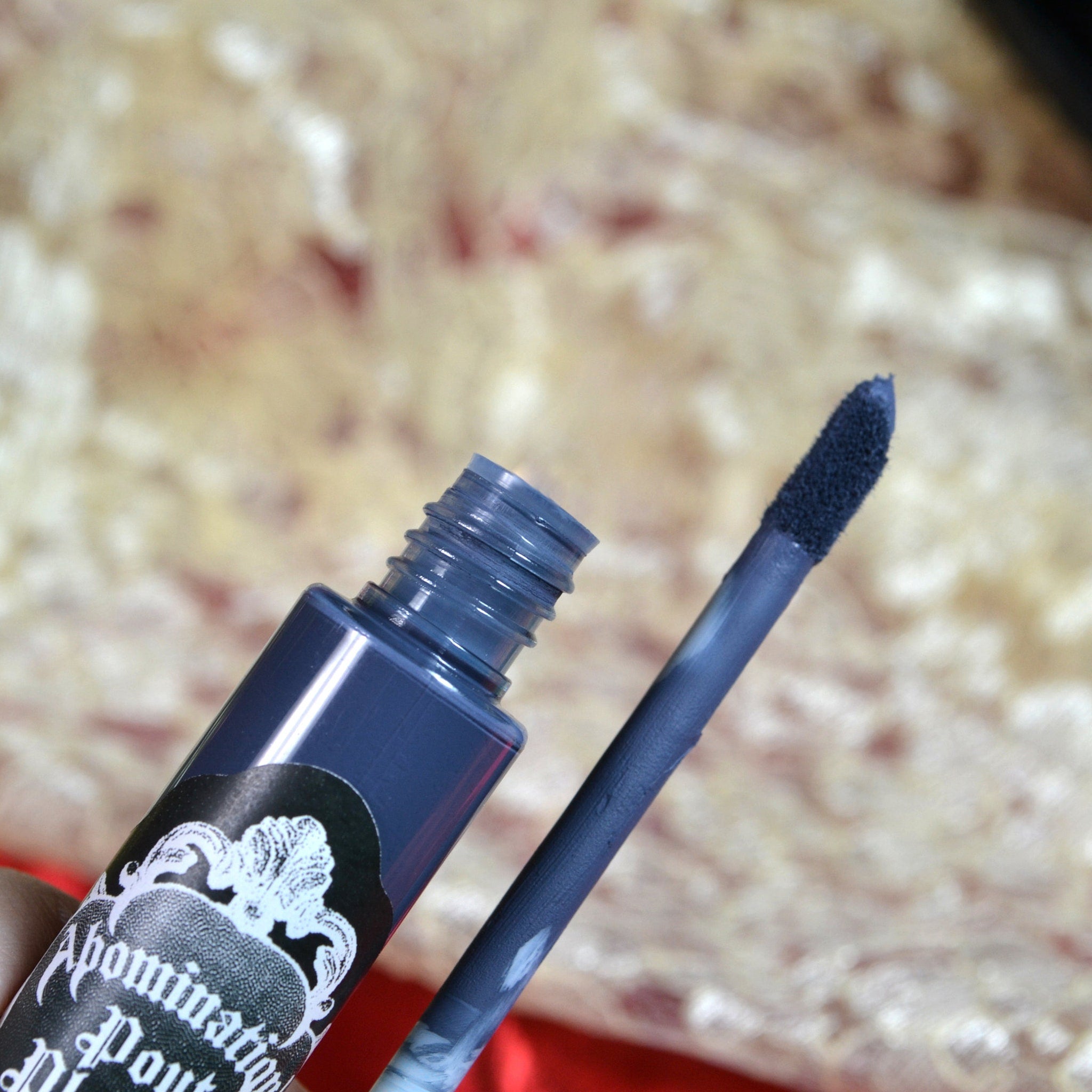 Blue lip gloss with applicator, brand name visible on label, open bottle