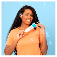 Facial cleanser tube held by woman, white tube with blue and green accents, ARTISTRY STUDIO branding