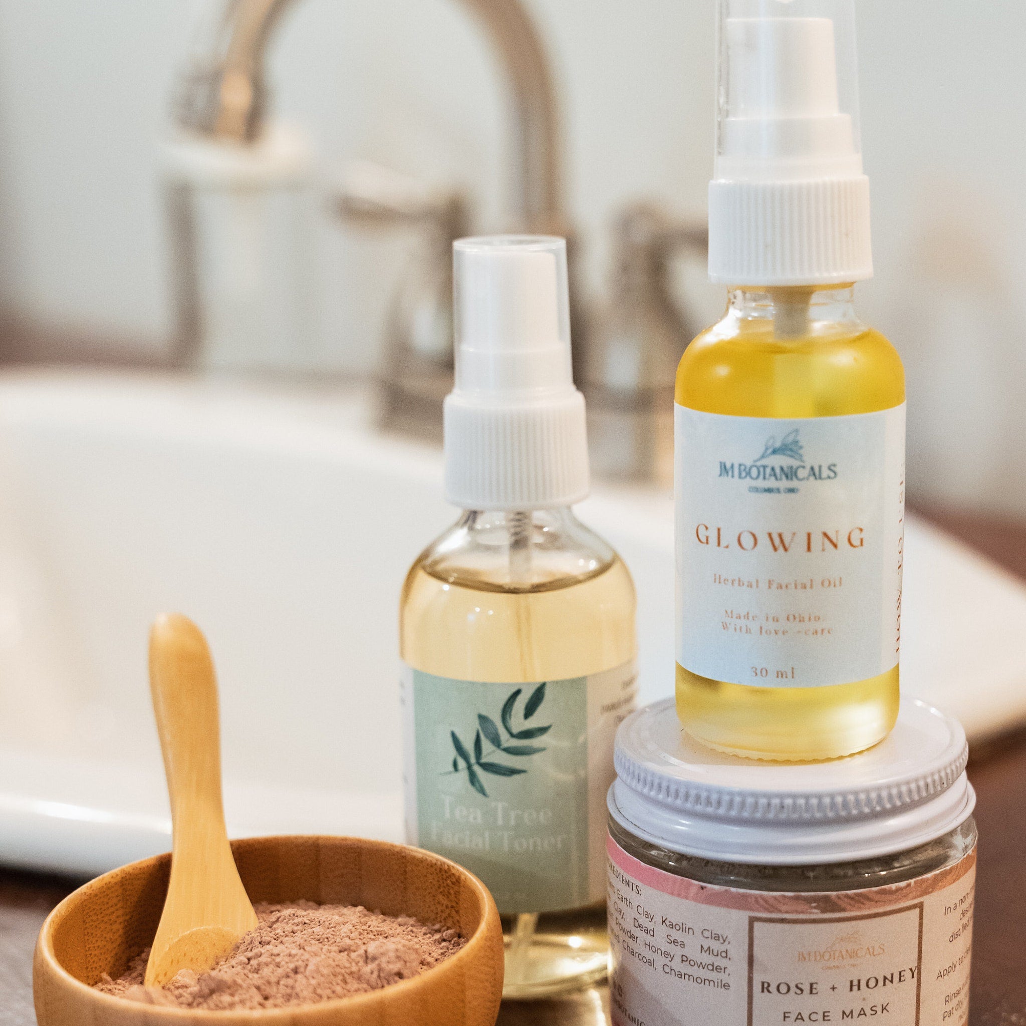Facial skincare products with glass bottles, wooden bowl, and JM Botanicals branding on a counter
