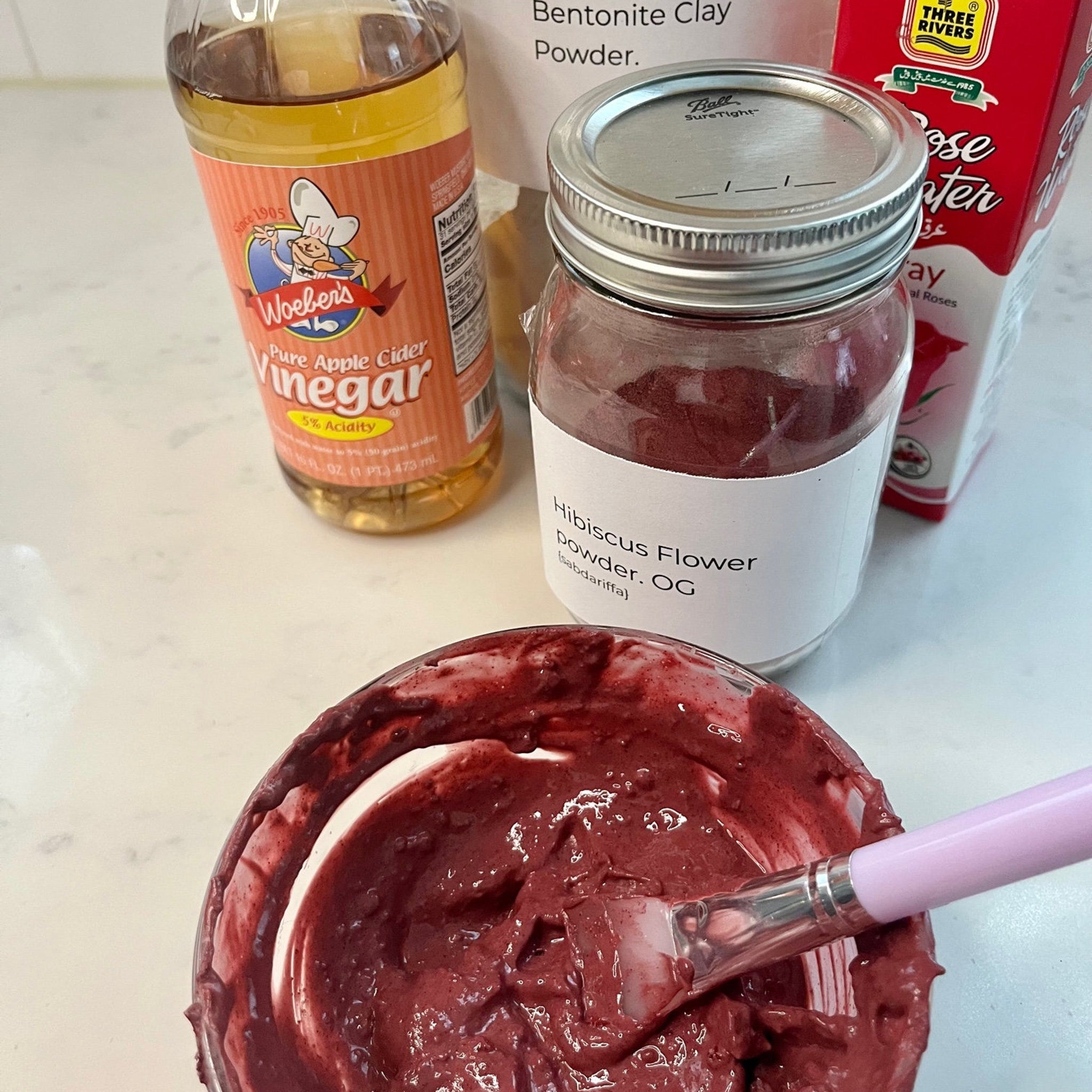 Face mask ingredients including red paste, clear glass jar, and Woebers apple cider vinegar bottle