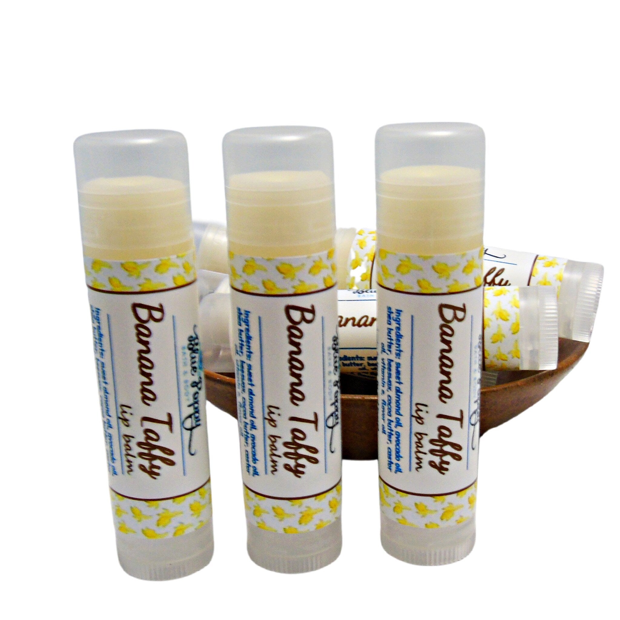 Lip balm tubes with white labels, yellow banana pattern, and clear caps, in wooden bowl