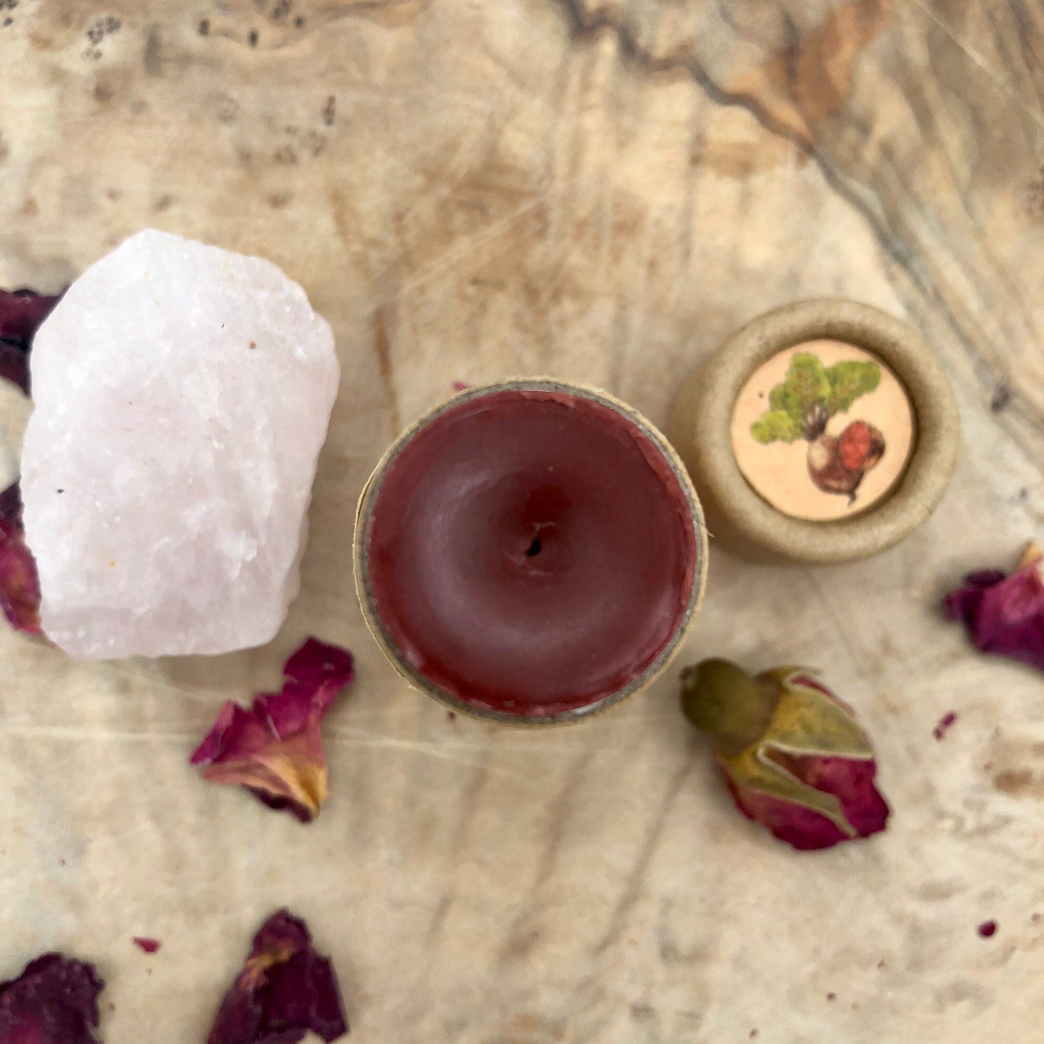 Candle with red wax, beige paper tube, and rose quartz crystal on wood surface