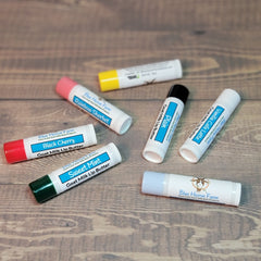 Lip butter tubes in various colors, with Blue Heron Farm branding visible on white tubes, on wood surface