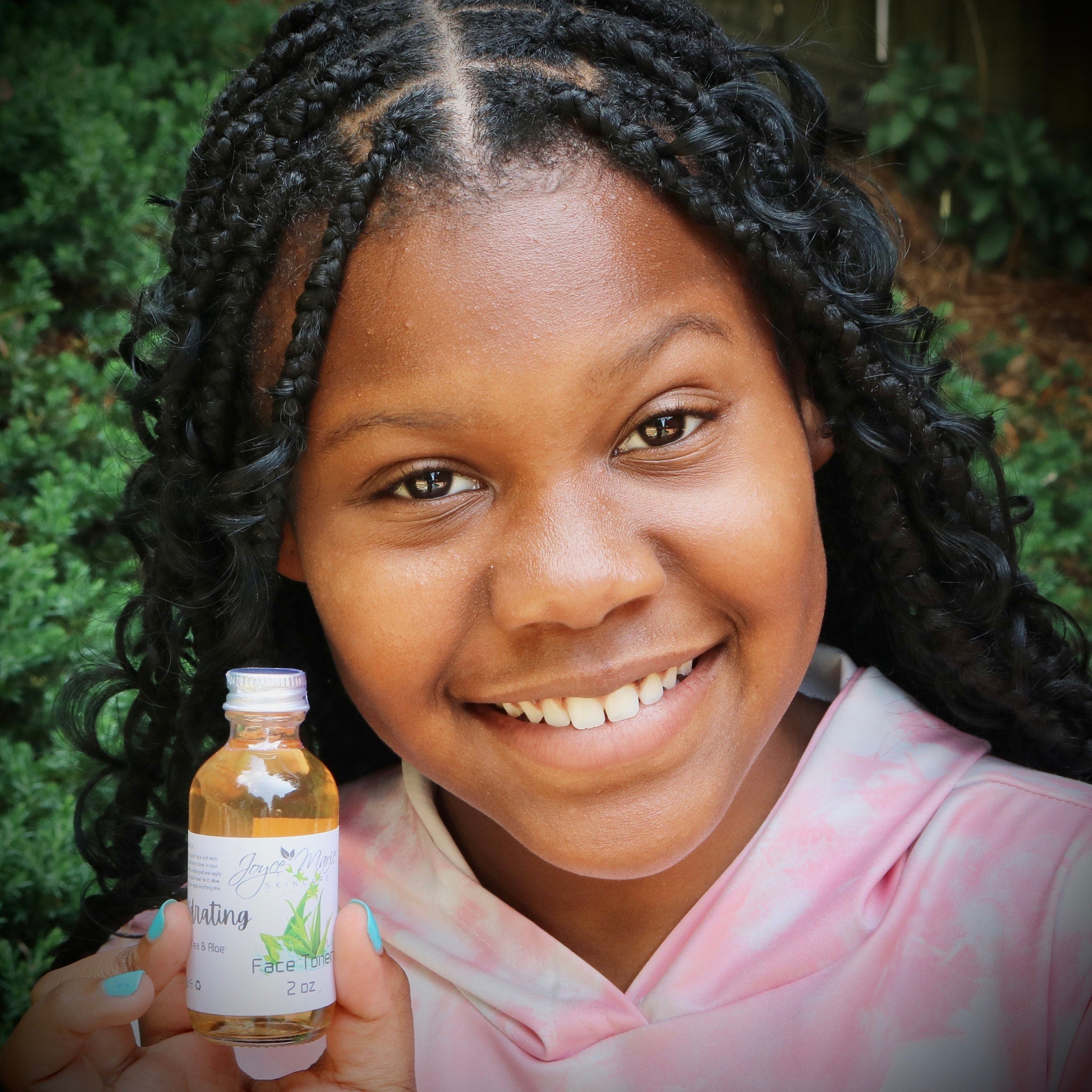 Face toner bottle held by person with black braids and tie-dye pink hoodie