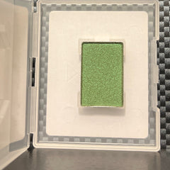 Close-up of fingertips applying shimmering emerald green mineral eye shadow to eyelid