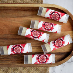 Lip balm tubes with red and white striped pattern, clear cap, and "Candy Cane Lip Balm" text on a wooden tray