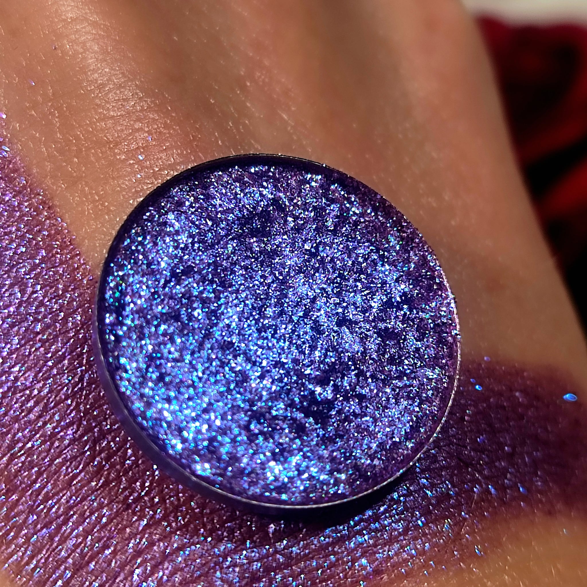 Eyeshadow compact with blue glitter and purple shimmer, shown on skin for color swatch