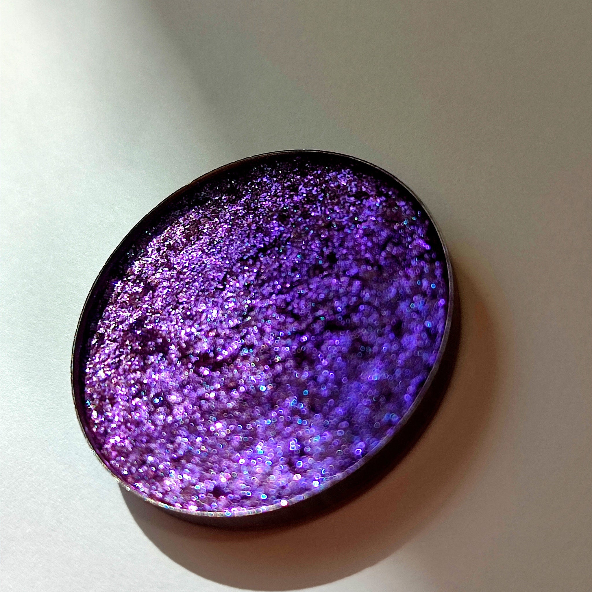 Close-up of Uva Eye Shadow pan showing shimmering purple pigment with smooth pressed texture