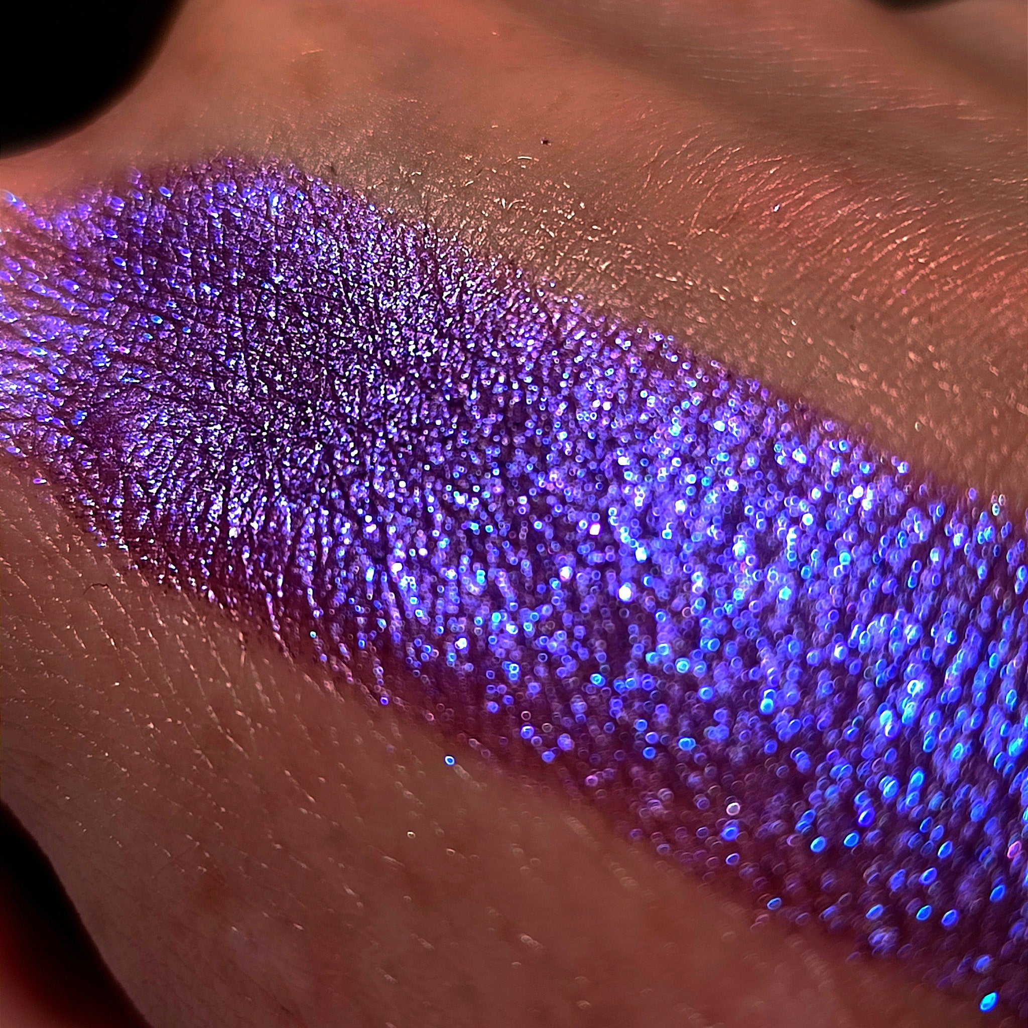 Purple eyeshadow swatch with glitter, iridescent shimmer, and skin background