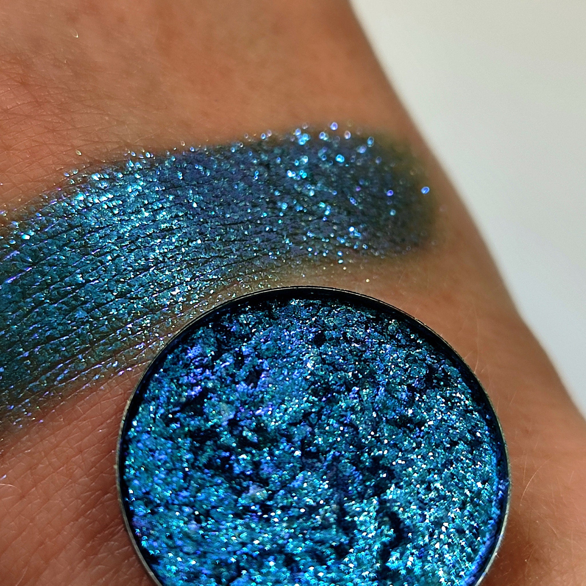 Eyeshadow compact with blue glitter, metallic finish, and swatch on skin
