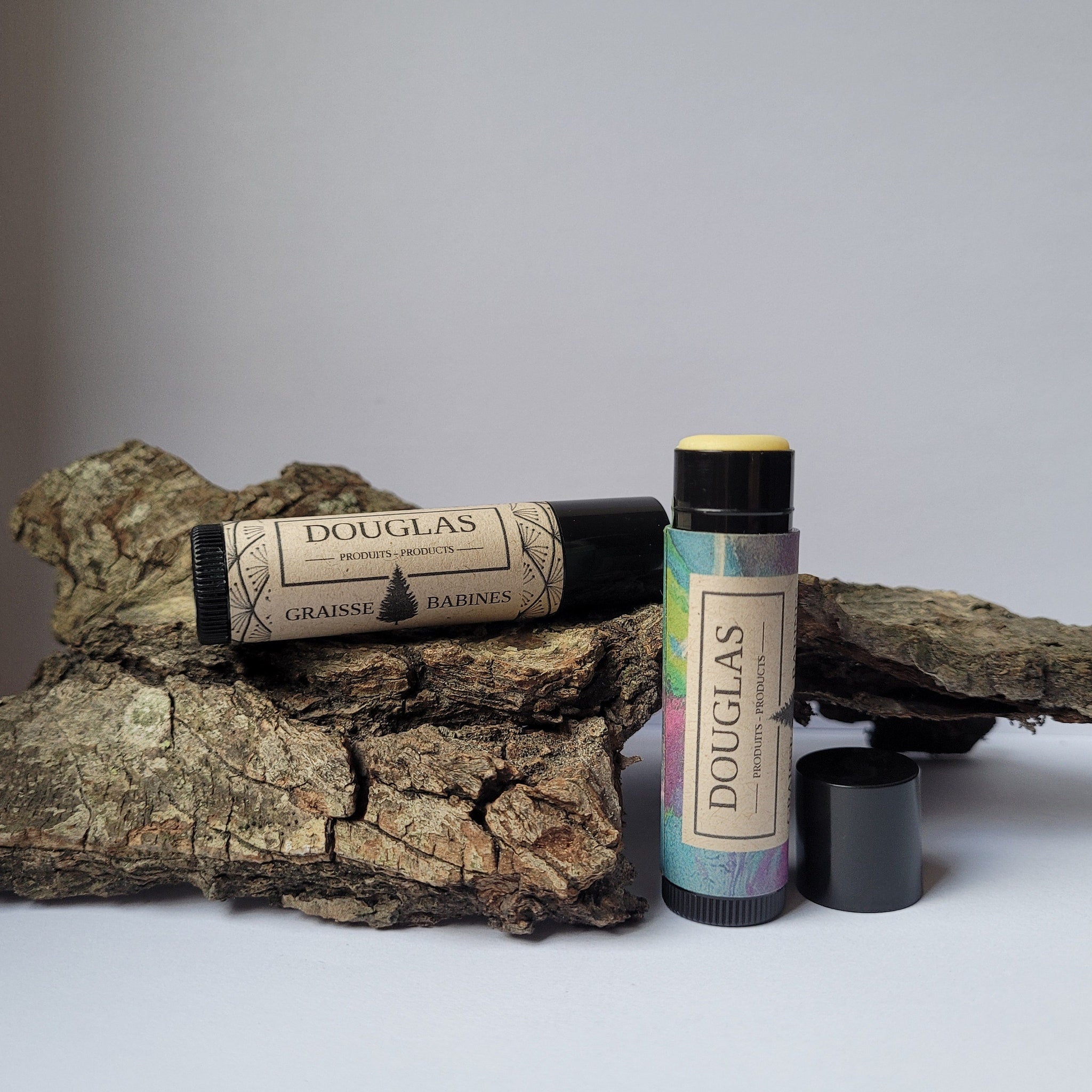 Lip balm tubes with black and patterned labels, Douglas branding visible, on wood bark