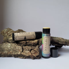 Lip balm tubes with black and patterned labels, Douglas branding visible, on wood bark