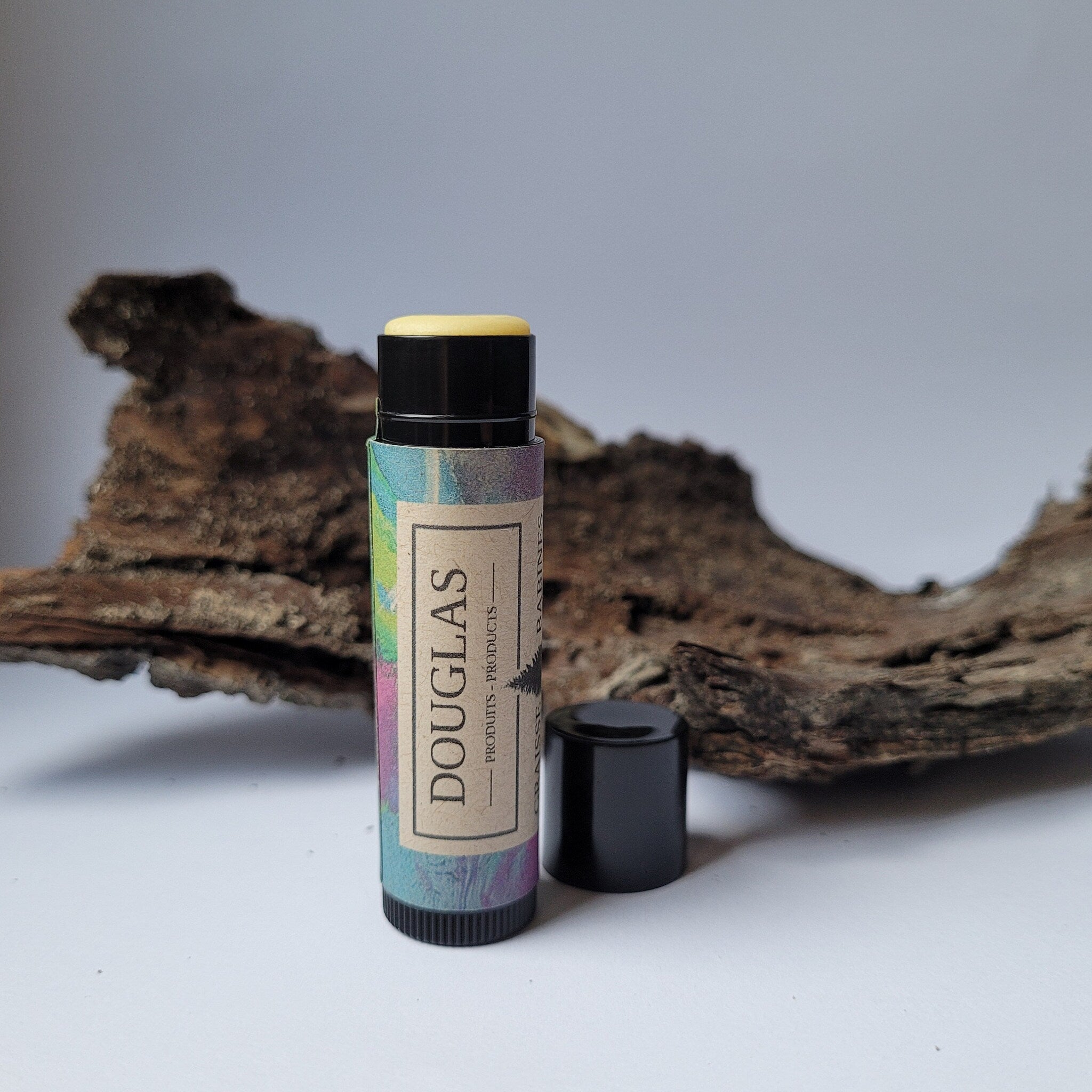 Lip balm tube with colorful label, black cap, and yellow balm visible, "DOUGLAS" text