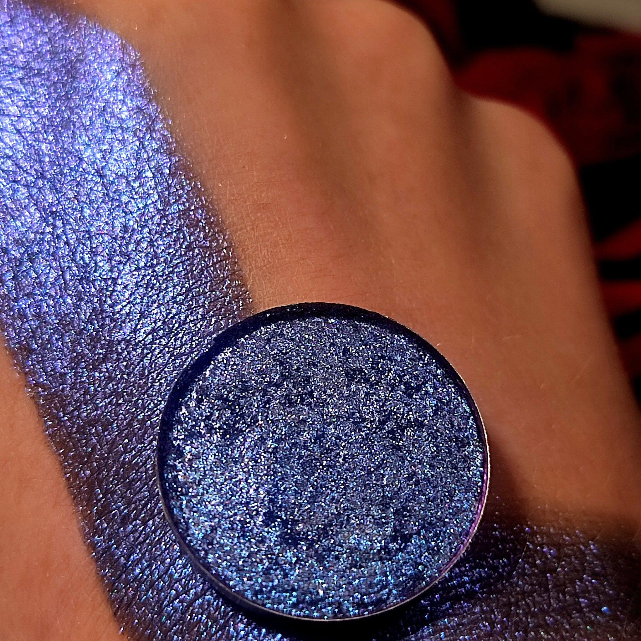 Eyeshadow swatch with blue glitter and metallic finish on skin, round compact shown