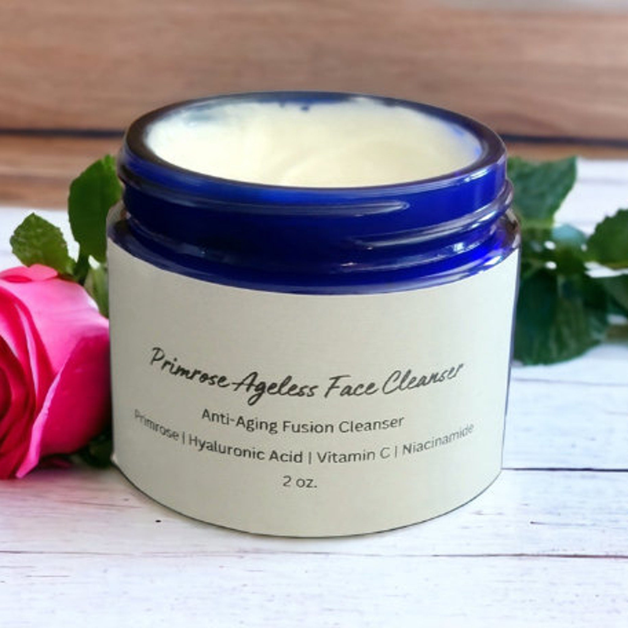Facial cleanser jar with blue rim, white label, and Primrose text, next to a pink rose