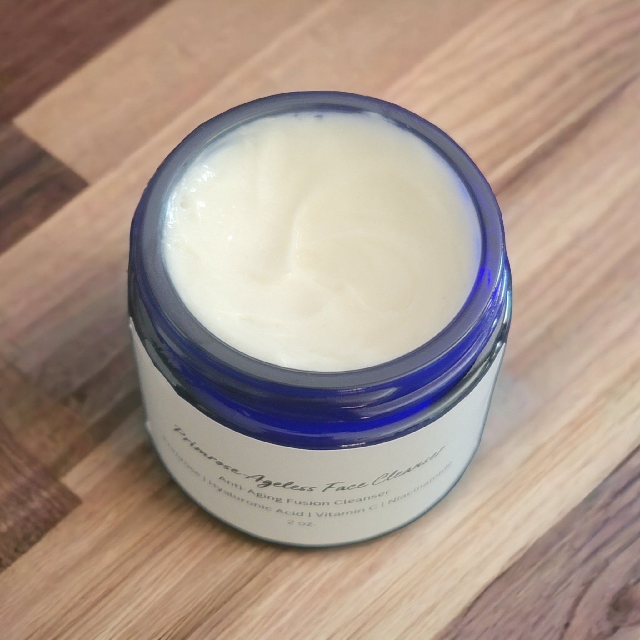 Face cleanser jar with white cream, blue rim, and Primrose label on wood surface