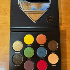 Eyeshadow palette with multiple colorful eyeshadows in a black compact with a mirror and text